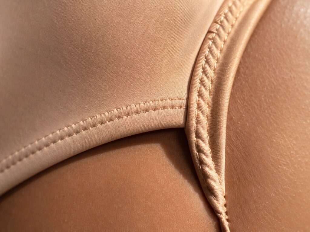 Macro close-up of swimwear fabric texture — lycra weave, stitching detail, and natural shadow at fabric edge